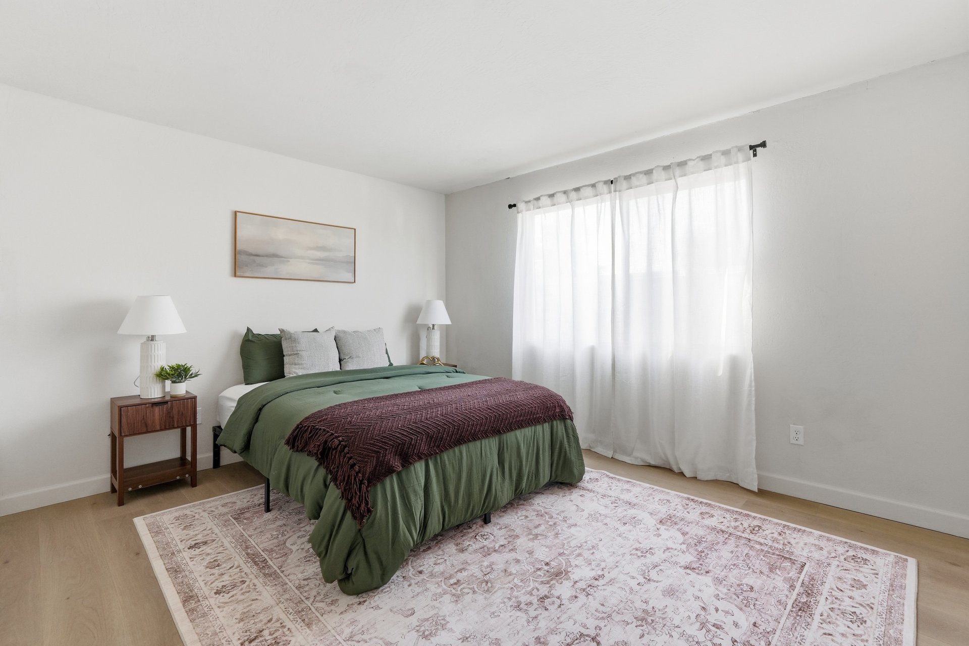 Second bedroom with a large curtained window and light wood flooring