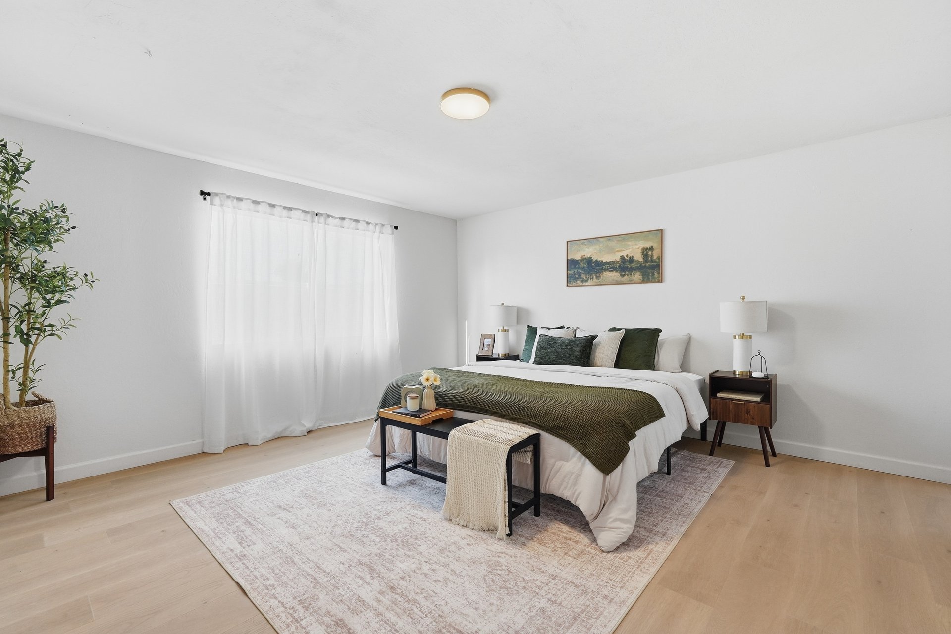 Primary bedroom with large window and light wood flooring