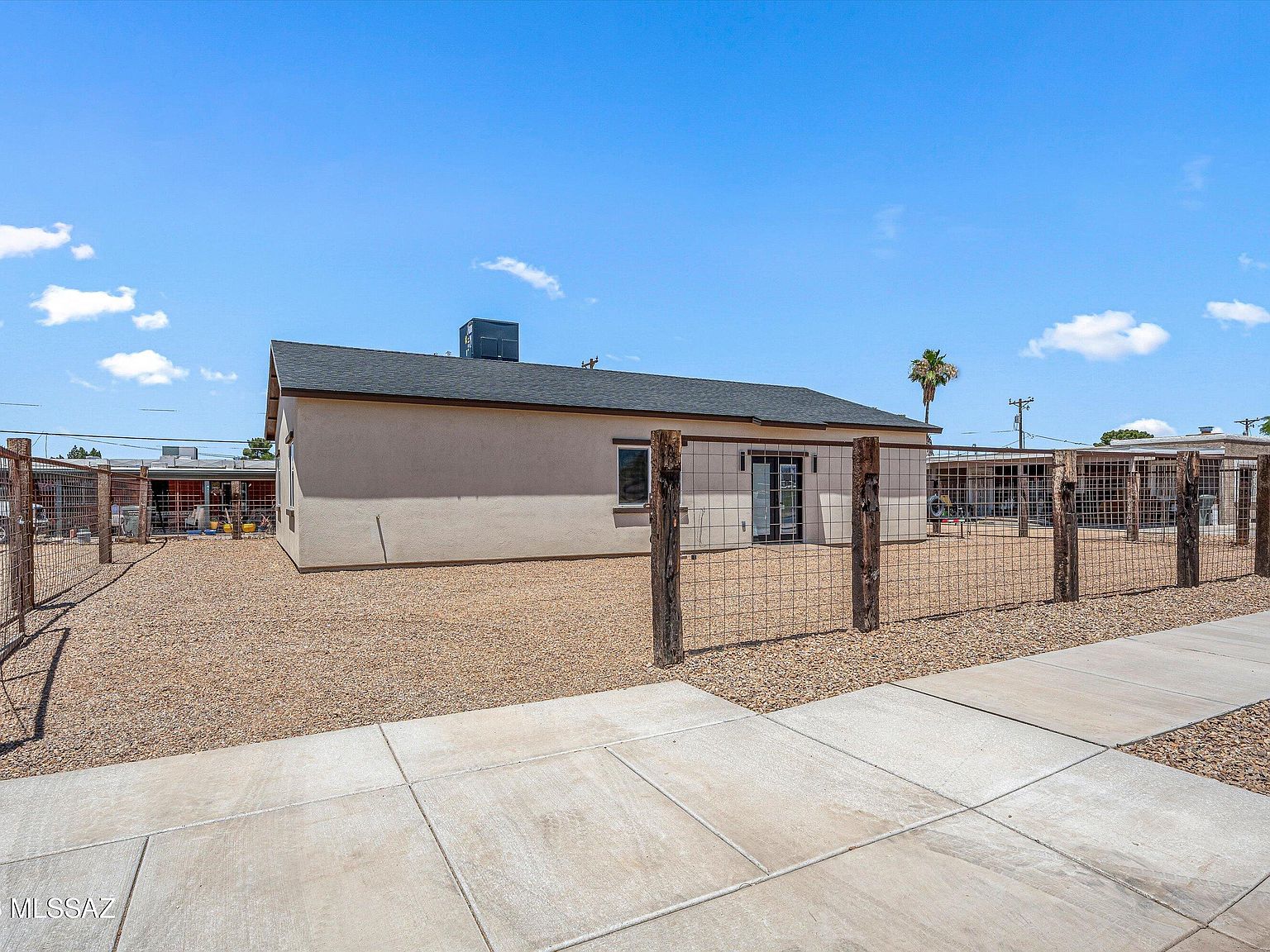 Single story new construction home with a fenced gravel yard under a blue sky